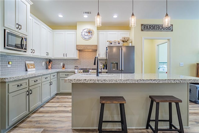 kitchen with visible vents, light wood-type flooring, decorative backsplash, appliances with stainless steel finishes, and a sink