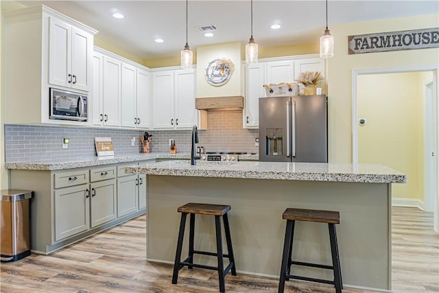 kitchen featuring visible vents, a breakfast bar, tasteful backsplash, appliances with stainless steel finishes, and light wood finished floors