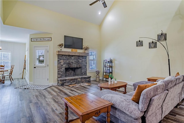 living area featuring a stone fireplace, a ceiling fan, wood finished floors, and high vaulted ceiling