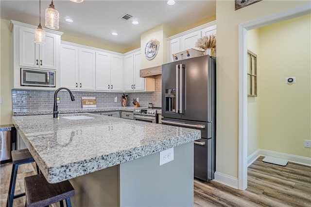 kitchen featuring visible vents, a sink, tasteful backsplash, appliances with stainless steel finishes, and a breakfast bar area