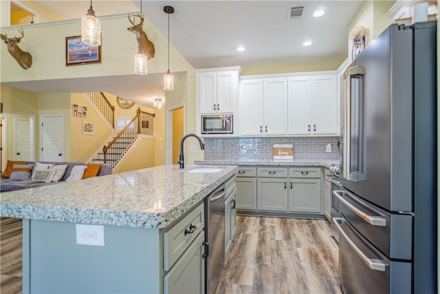 kitchen featuring visible vents, light wood-style flooring, a sink, decorative backsplash, and stainless steel appliances