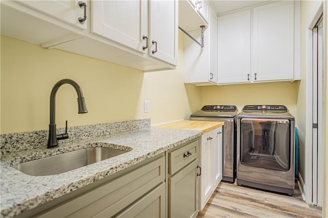 laundry room with cabinet space, washer and dryer, light wood-type flooring, and a sink