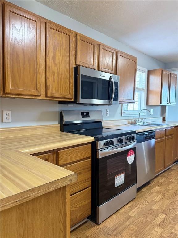 kitchen with sink, butcher block countertops, appliances with stainless steel finishes, and light wood-type flooring