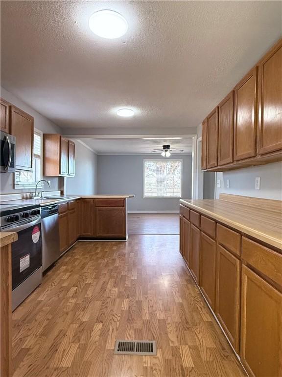 kitchen with ceiling fan, a textured ceiling, appliances with stainless steel finishes, and light wood-type flooring