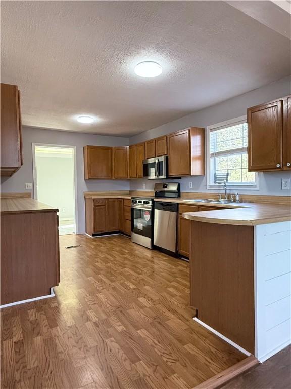 kitchen with kitchen peninsula, sink, light hardwood / wood-style floors, and appliances with stainless steel finishes