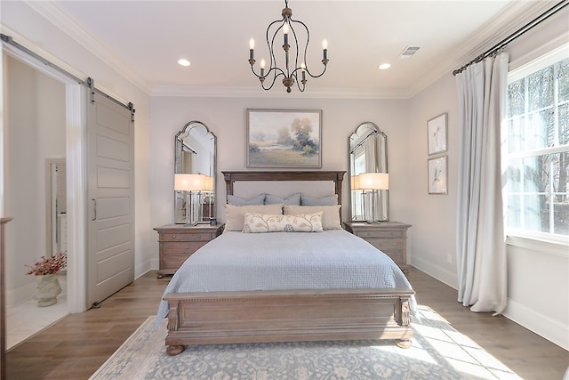 bedroom with a barn door, visible vents, crown molding, and wood finished floors