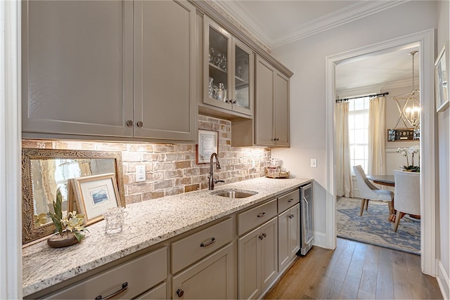 kitchen featuring a sink, ornamental molding, light wood-type flooring, decorative backsplash, and glass insert cabinets