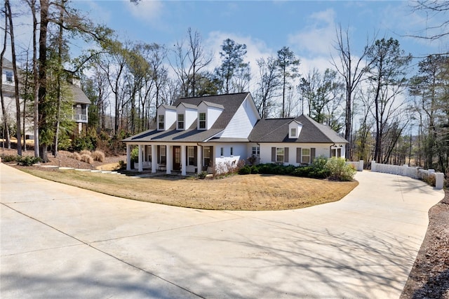 new england style home featuring a porch, concrete driveway, and a front lawn