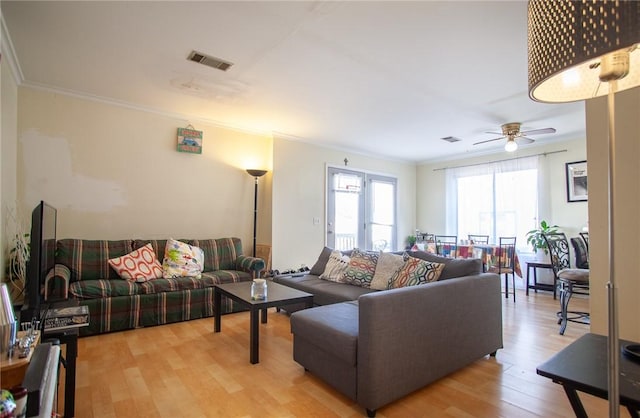 living area with light wood-type flooring, a ceiling fan, visible vents, and crown molding