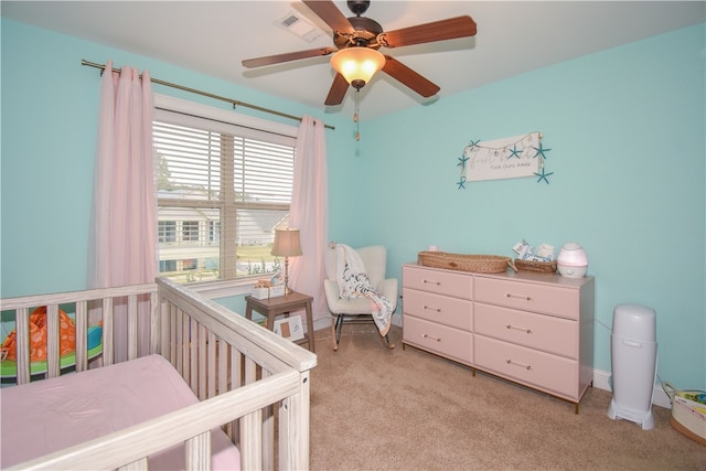 bedroom featuring a nursery area, light carpet, and ceiling fan