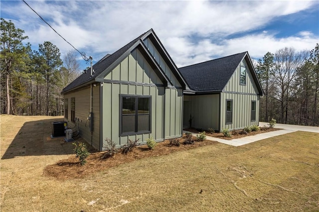 view of front of home with a shingled roof, board and batten siding, cooling unit, and a front lawn