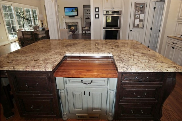 kitchen with dark brown cabinetry, light stone counters, a kitchen island, and stainless steel double oven