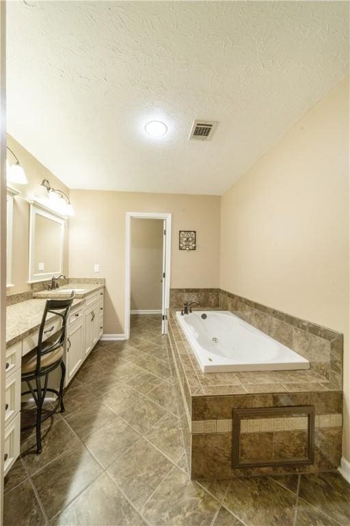 bathroom featuring a relaxing tiled tub, a textured ceiling, and vanity