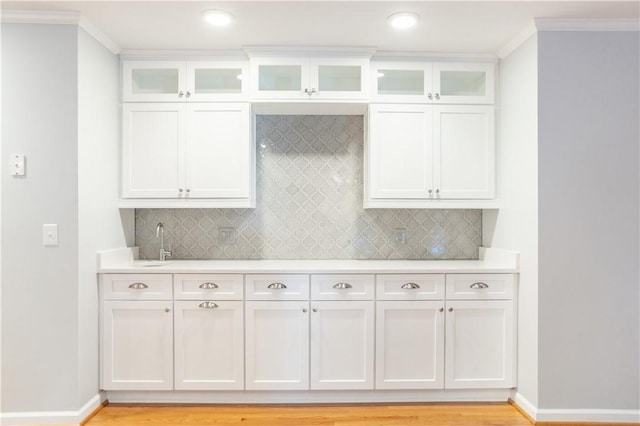 kitchen featuring tasteful backsplash, ornamental molding, sink, light hardwood / wood-style flooring, and white cabinets