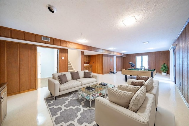 living room featuring a textured ceiling, wooden walls, and pool table