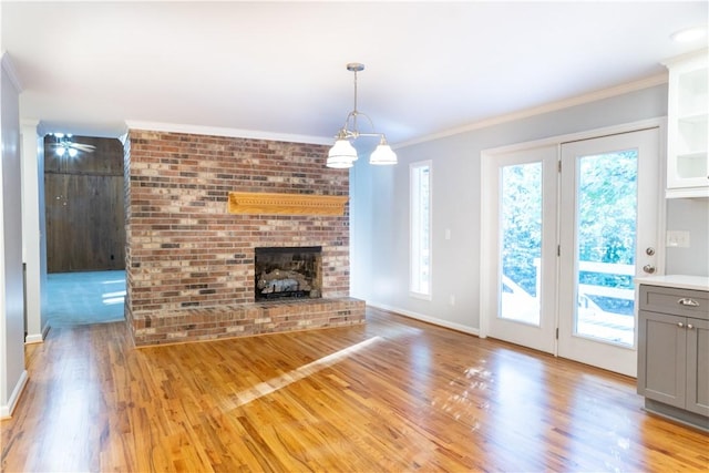 unfurnished living room featuring light wood-type flooring, crown molding, a wealth of natural light, and a brick fireplace