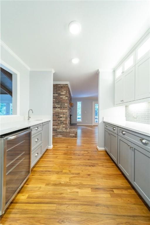 interior space with wine cooler, crown molding, decorative backsplash, and light wood-type flooring