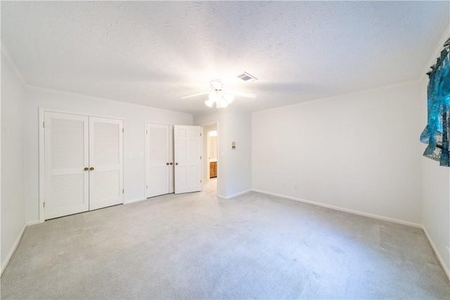 unfurnished bedroom with light carpet, a textured ceiling, ceiling fan, and multiple closets