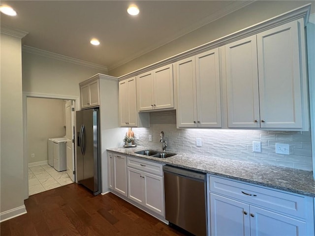 kitchen with a sink, light stone counters, washer and dryer, crown molding, and appliances with stainless steel finishes