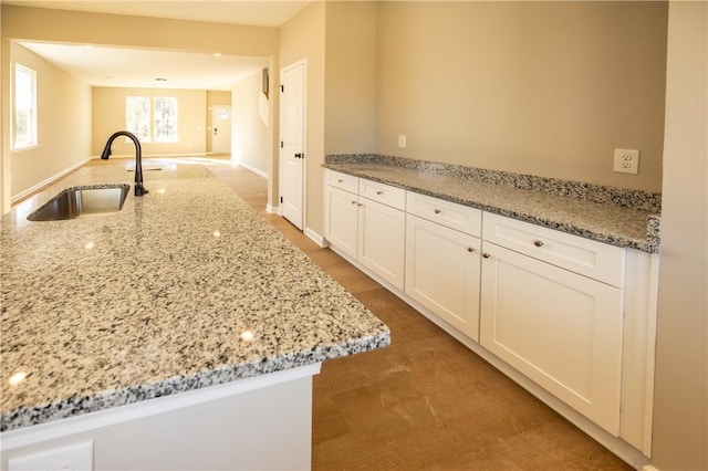 kitchen with white cabinets, a center island with sink, light stone counters, and sink