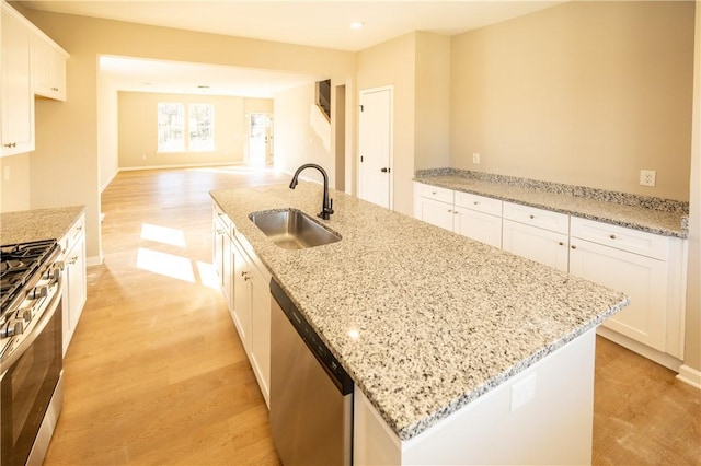 kitchen with a kitchen island with sink, white cabinets, sink, light stone countertops, and appliances with stainless steel finishes