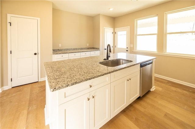 kitchen with dishwasher, sink, light stone counters, a kitchen island with sink, and white cabinets