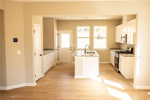 kitchen with white cabinets, appliances with stainless steel finishes, a kitchen island with sink, and sink