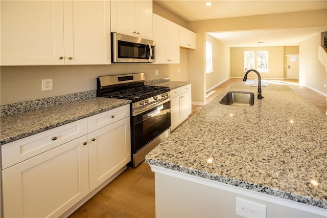 kitchen featuring white cabinets, stainless steel appliances, light stone counters, and sink