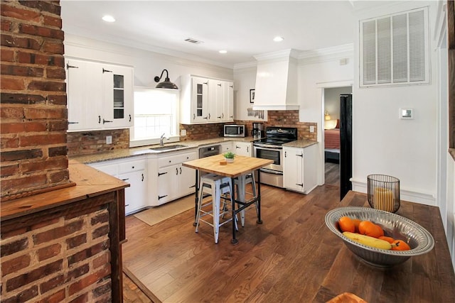kitchen with a sink, appliances with stainless steel finishes, wooden counters, custom exhaust hood, and decorative backsplash