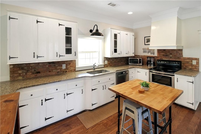 kitchen with premium range hood, dark wood-style flooring, stainless steel appliances, a sink, and visible vents