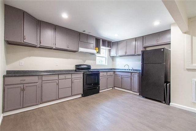 kitchen with light wood finished floors, a sink, black appliances, and dark countertops