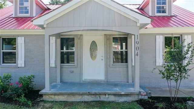 entrance to property featuring brick siding, a porch, and metal roof