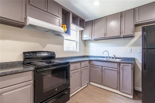 kitchen featuring light wood-type flooring, black appliances, under cabinet range hood, a sink, and dark countertops
