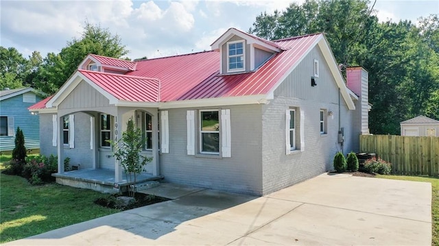 view of front of property featuring covered porch, metal roof, fence, brick siding, and a chimney