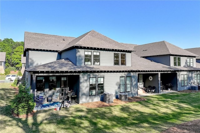 back of property with cooling unit, a yard, a shingled roof, and a patio