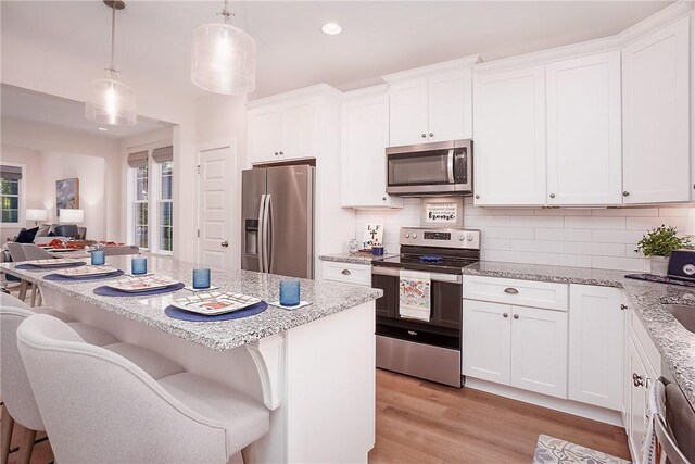 kitchen with tasteful backsplash, light stone countertops, stainless steel appliances, and white cabinetry