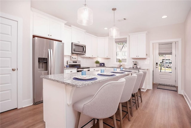 kitchen with light wood finished floors, stainless steel appliances, a center island, visible vents, and backsplash
