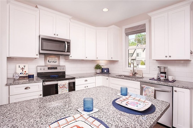 kitchen featuring white cabinets, a sink, decorative backsplash, light stone counters, and appliances with stainless steel finishes