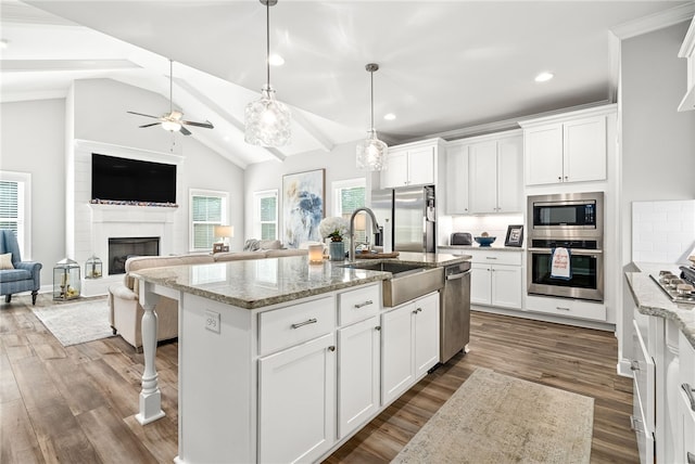 kitchen with a sink, stainless steel appliances, a fireplace, lofted ceiling with beams, and ceiling fan