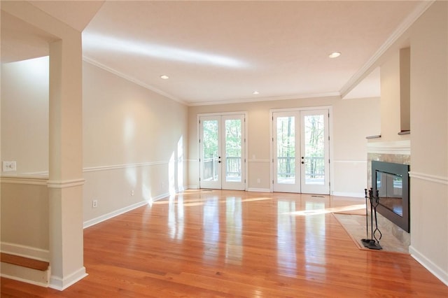 unfurnished living room with ornamental molding, french doors, light wood-type flooring, and a fireplace