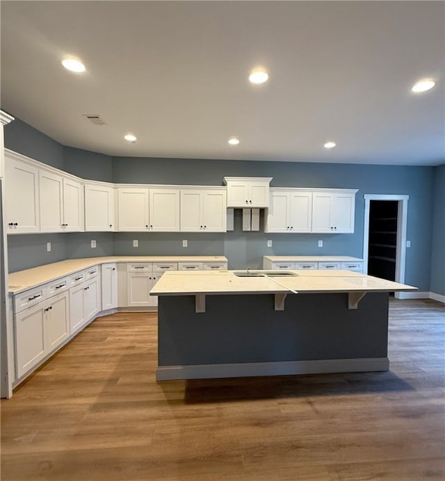 kitchen with white cabinetry, hardwood / wood-style floors, a kitchen breakfast bar, and an island with sink