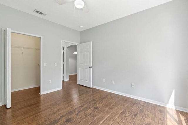 unfurnished bedroom featuring ceiling fan, dark hardwood / wood-style floors, a closet, and a walk in closet