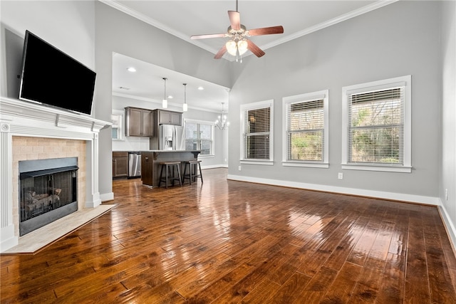 unfurnished living room with crown molding, ceiling fan with notable chandelier, dark hardwood / wood-style floors, and a towering ceiling