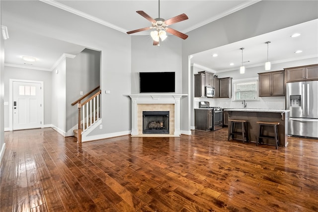 unfurnished living room featuring dark hardwood / wood-style floors, sink, a tiled fireplace, ceiling fan, and crown molding