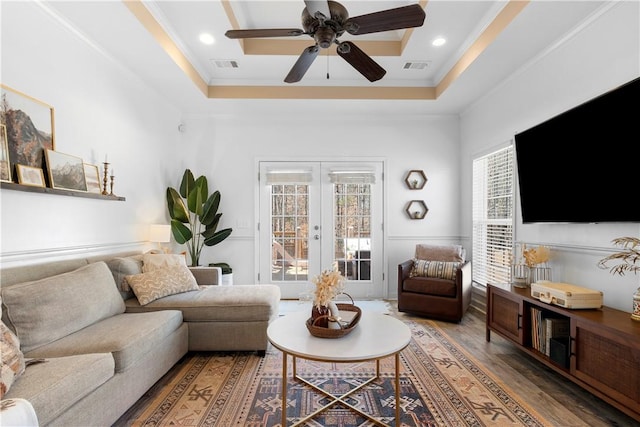 living room with a tray ceiling, wood finished floors, french doors, and visible vents