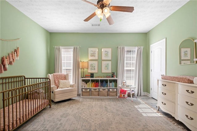 bedroom featuring visible vents, multiple windows, a textured ceiling, and a crib