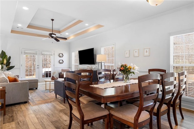 dining room with french doors, a raised ceiling, ornamental molding, and light wood finished floors