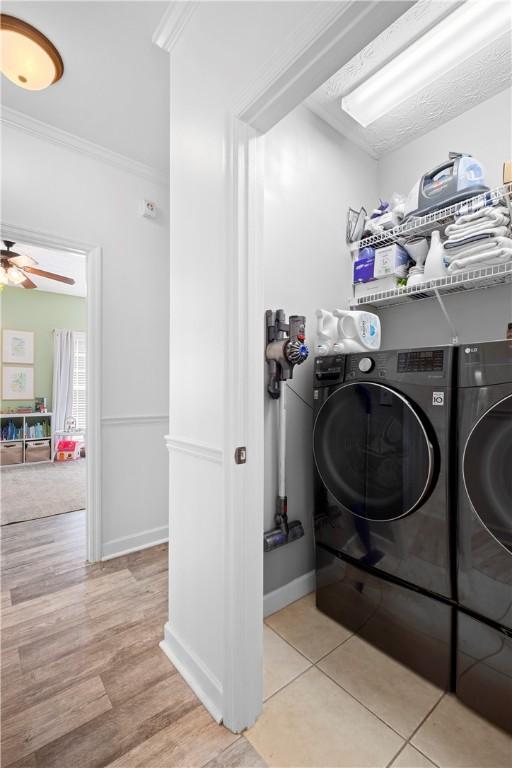 clothes washing area with a ceiling fan, washer and dryer, light wood-style floors, crown molding, and laundry area