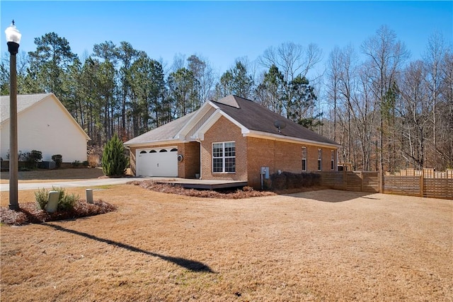 view of side of home with a garage, fence, brick siding, and driveway