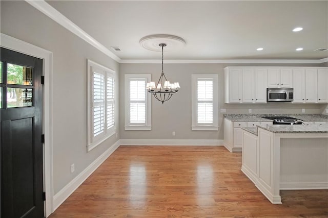 2904 Lone Eagle Ln, Opelika, AL 36801 - kitchen with stainless steel microwave, a chandelier, white cabinets, light wood-style flooring, and ornamental molding